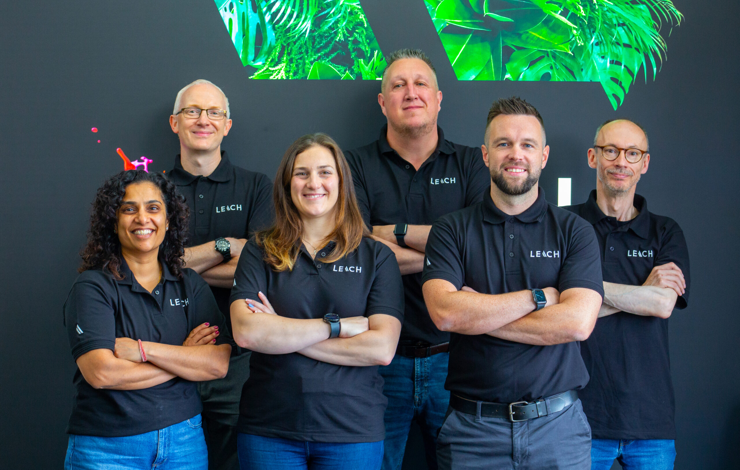 6 members of the Leach team, stood in front of a black graphic