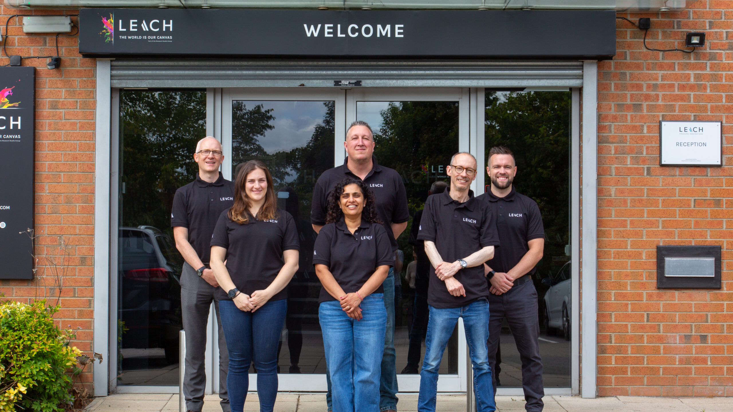 6 members of the Leach team, stood in front of an entrance, with the word Welcome above them