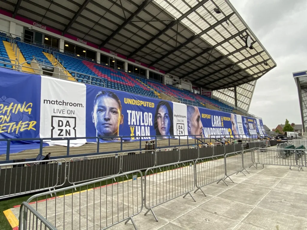 Boxing event graphics displayed at the stadium. It features fighters. The theme is matching stadium colours- it is blue, white and yellow