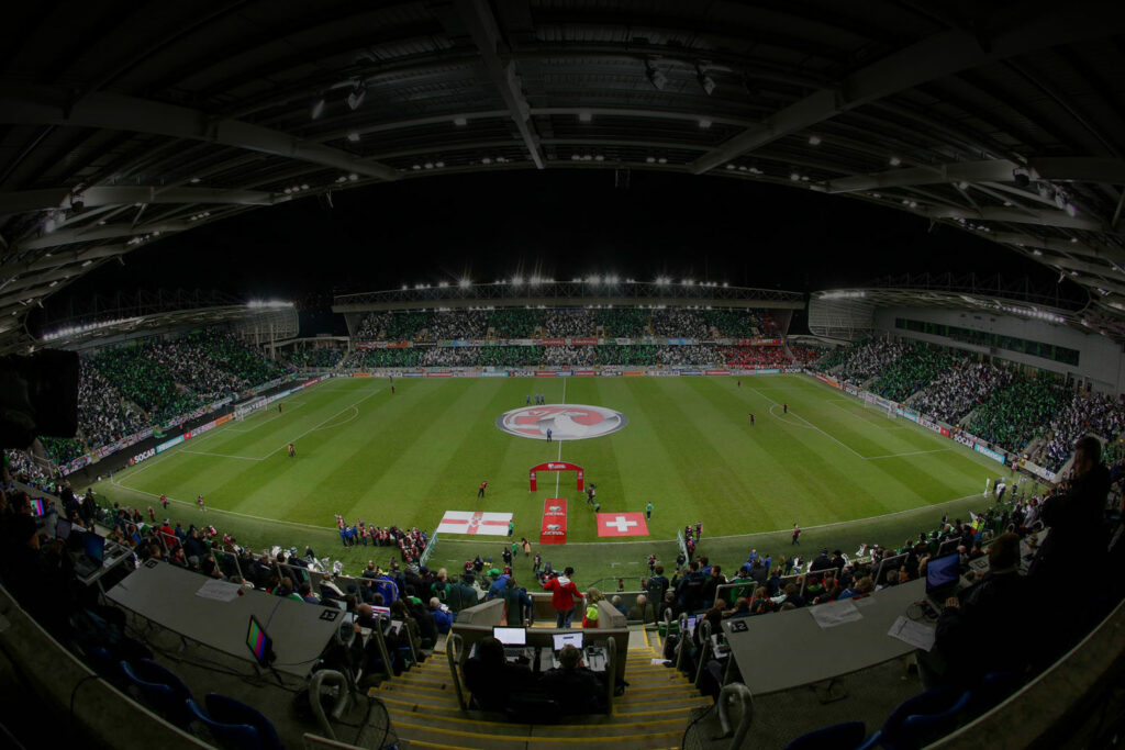 Inside of a sports stadium, with printed flags of Northern Ireland and Switzerland laid on the pitch