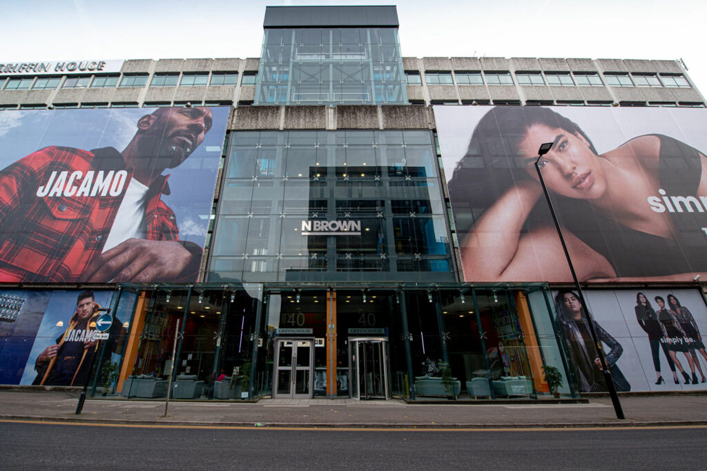 Huge, creative construction branding canvas is covering the building behind it. Large format print features a man in red checked jacket and woman wearing black top.