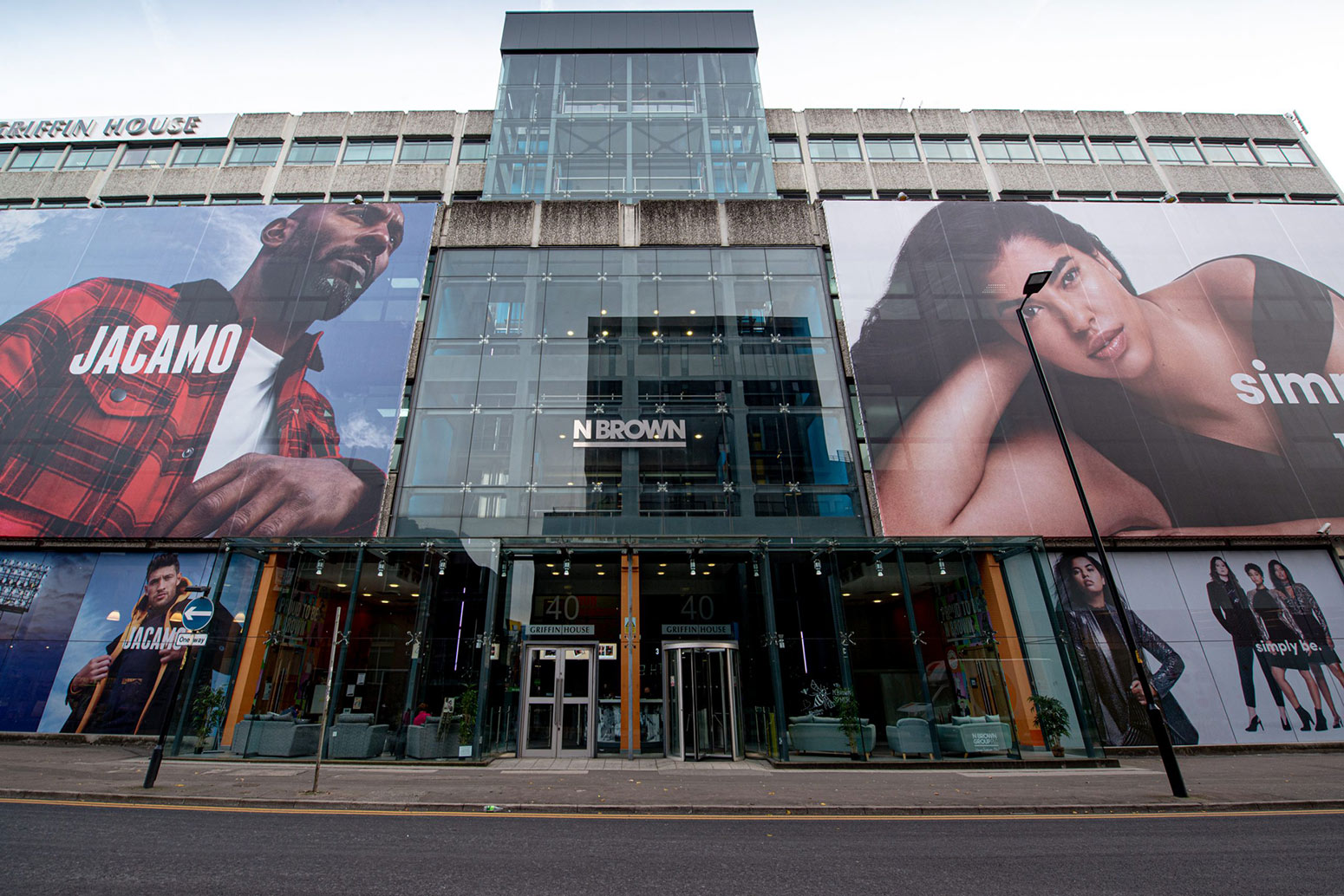 Huge, creative construction branding canvas is covering the building behind it. Large format print features a man in red checked jacket and woman wearing black top.