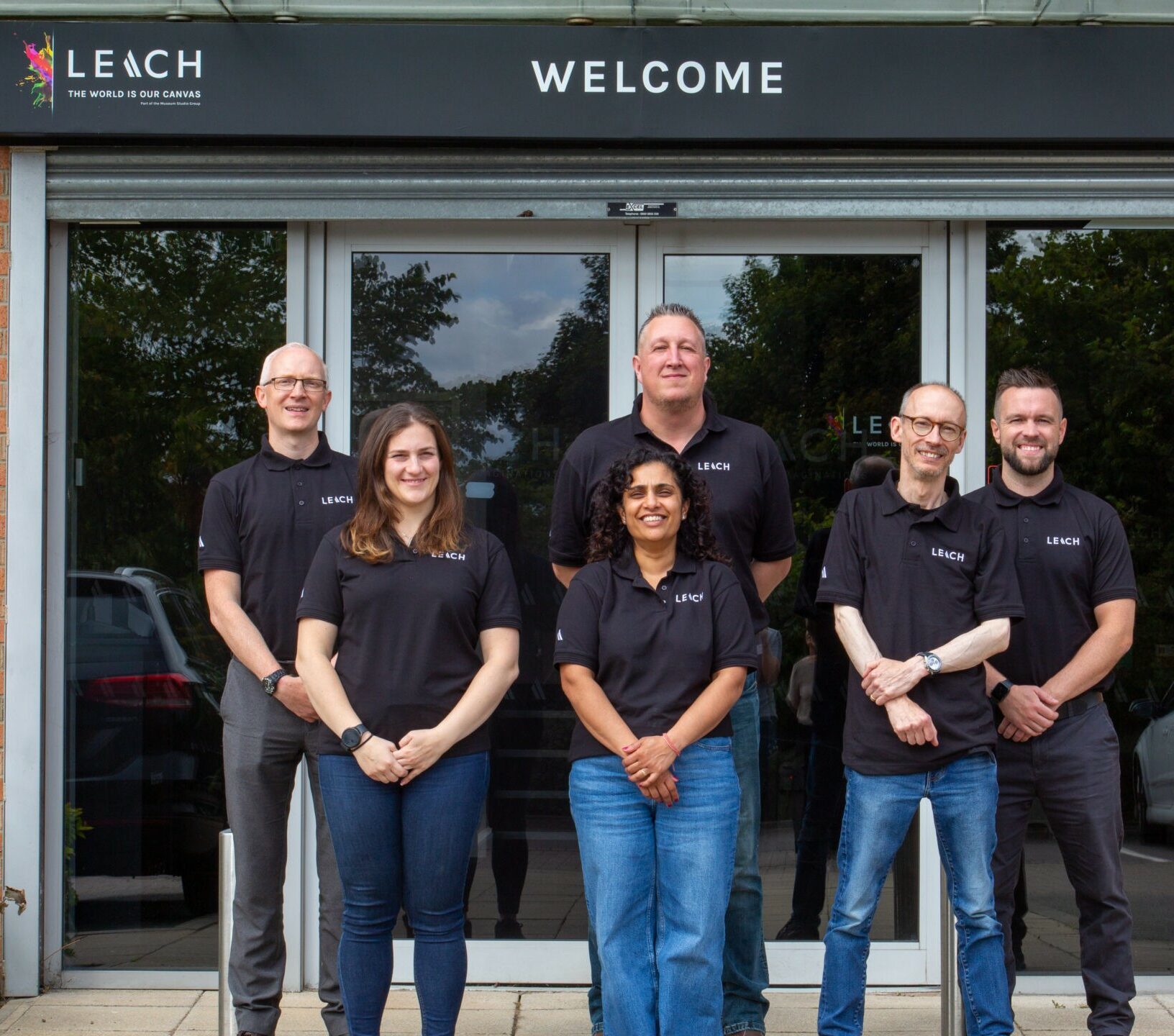 6 members of the Leach team, stood in front of an entrance, with the word Welcome above them